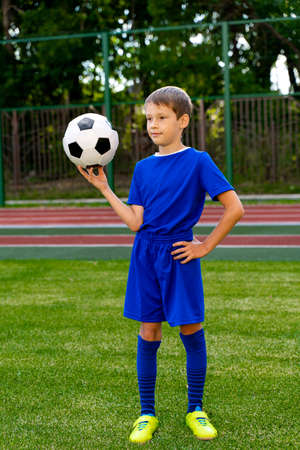 a small football player with a ball stands on a green football fieldの写真素材