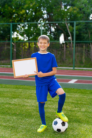 a small soccer player with a ball stands on a green soccer field with a white piece of writing paperの写真素材