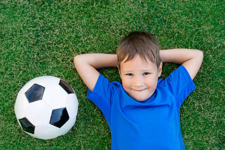 A little boy lies on a green soccer field, a soccer ball, top viewの写真素材