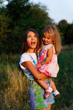 beautiful mom and daughter play with Hol colors. multi-colored paint on clothes and faceの写真素材