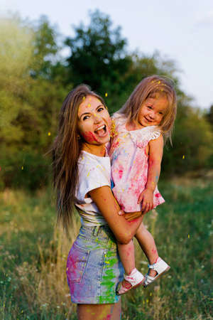 beautiful mom and daughter play with Hol colors. multi-colored paint on clothes and faceの写真素材