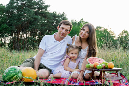 beautiful family, mom, dad and daughter sitting on a picnic with watermelonの写真素材