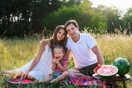beautiful family, mom, dad and daughter sitting on a picnic with watermelonの写真素材
