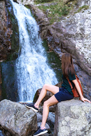 Active healthy girl tourist sitting near the waterfall.の写真素材