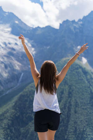a girl stands in the mountains and raises her hands to the skyの写真素材