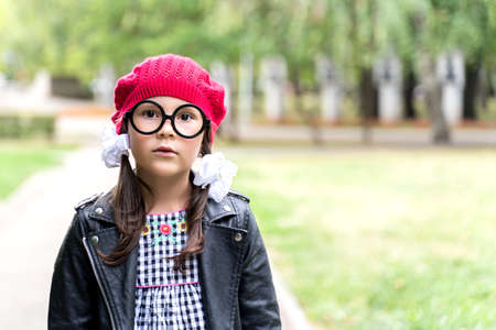 a little funny girl in a red cap and round glasses looks into the frame.の写真素材