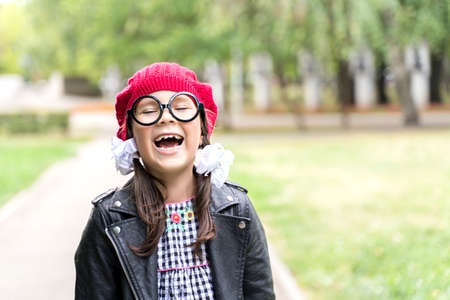 a funny little girl in a red cap and round glasses laughs.の写真素材