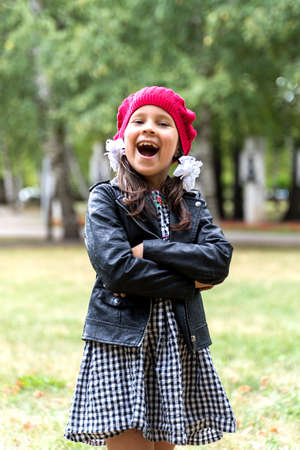 a funny little girl in a red cap is laughing with her arms crossed over her chest.の写真素材