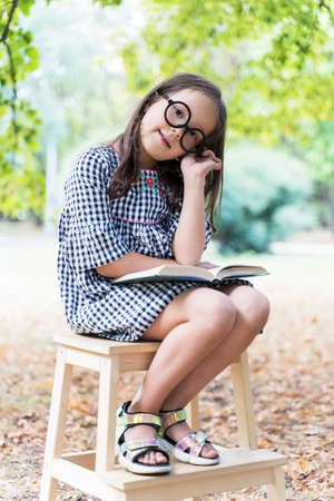 a little funny girl with glasses reads a book in natureの写真素材