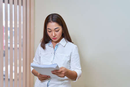 Asian Woman doctor in white coat reads medical documents.の写真素材