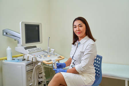Asian woman doctor ultrasound in a white coat next to the ultrasound machine.の写真素材