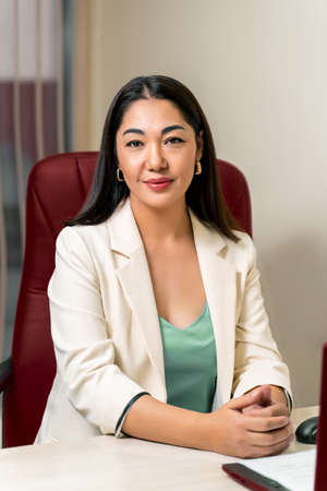 Asian female doctor in white coat sitting in red chair.の写真素材
