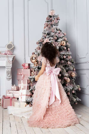 little girl in beautiful dress decorates Christmas treeの写真素材