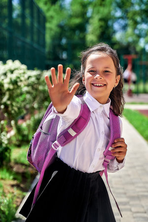 a schoolgirl girl in a white shirt with a backpack at school shows her palm five