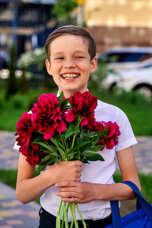 a beautiful schoolboy with a backpack on a holiday at school with flowersの写真素材