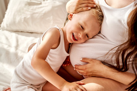 little son and his pregnant mother hug together.