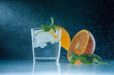 Fresh lemonade with mint, orange and ice in a glass jar on a dark blue background. Splashing water...