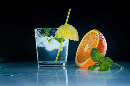Fresh lemonade with mint, orange and ice in glass jar on the dark background. On a mirror surface....