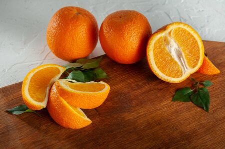 whole and slices of oranges with green leaves lie on a wooden board on a white background. Bright oranges over looking from above. Close-up and top view, flatlayの写真素材