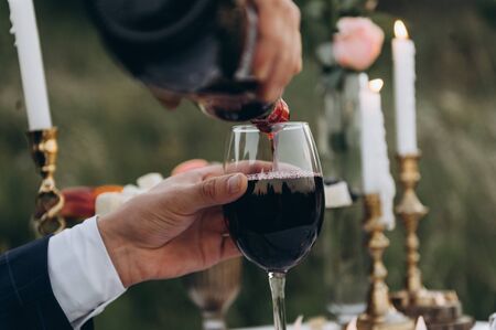 male hand pours wine into a glass at a romantic candlelight dinner, outsideの写真素材