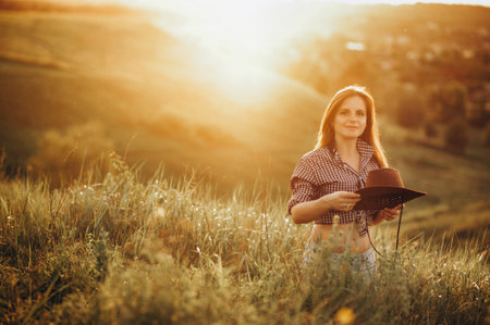 young girl in a field at sunset in a shirt and cowboy hat