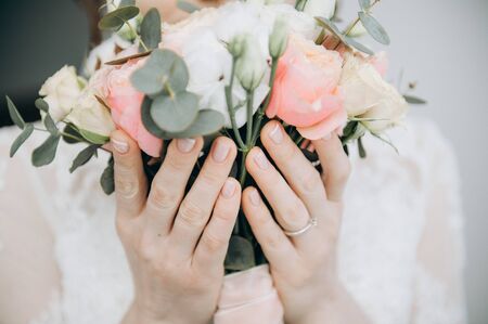 Very nice florist woman holding a beautiful colourful blossoming flower bouquet of fresh Quicksand roses, carnations, ranunculus, peony, pistachio leaves on the light wall backgroundの写真素材