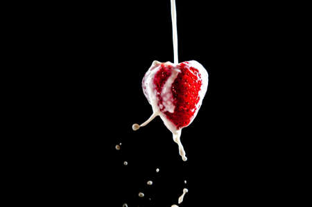 strawberry in the shape of a heart with cream on a dark background isolateの写真素材