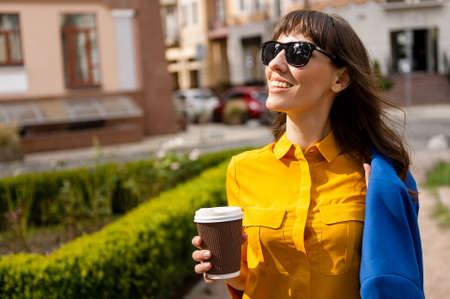 Summer sunny lifestyle fashion portrait of young stylish hipster woman walking on street,wearing cute trendy outfit,drinking hot latte,smiling enjoy weekends,travel with backpack,coffee,rest,loungeの写真素材