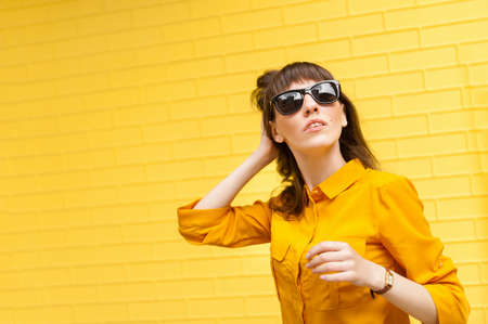 Young girl on bright yellow background in yellow shirt straightens her hairの写真素材