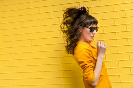 beautiful girl in a yellow shirt against the yellow wall. There is an empty space for inscription and textの写真素材