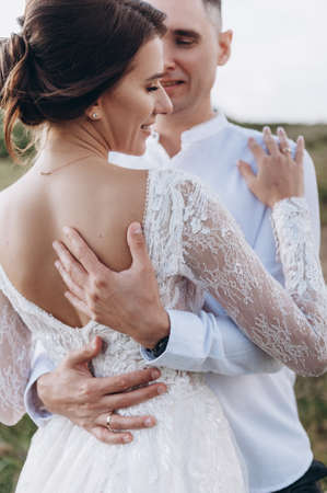 Bride in white dress stands with her back, her groom hugs herの写真素材