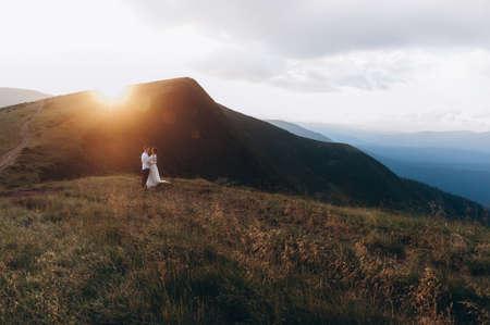 Newlyweds stand hugging against the background of the mountains at sunsetの写真素材