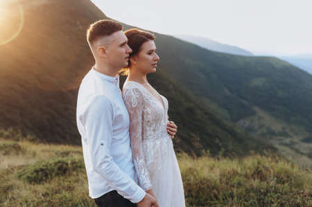 Newlyweds stand hugging against the backdrop of the mountainsの写真素材