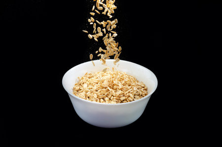 beautiful photo of oatmeal grains flying into a plate on a black backgroundの写真素材