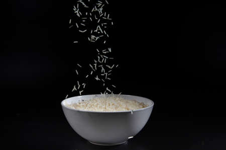 rice falls into a white plate on a black backgroundの写真素材