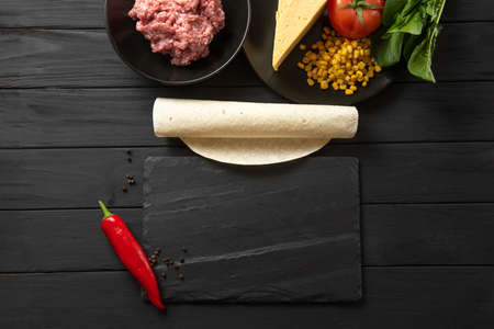 The ingredients for the traditional Latino American dish enchiladas are arranged on a dark background top view. Enchiladas are a traditional Mexican and South American cuisineの写真素材