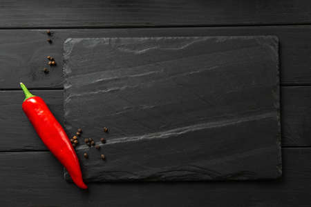 square slate board in dark color. chili peppers and spices on black background layout with space for text, top view flat layの写真素材