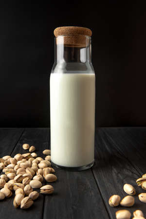 Pistachio milk in a bottle on a black background. vertical frame. Useful drink for a healthy diet. Pistachio milk contains B vitamins, vitamin K, vitamin A. Pistachio milk on a black background. A vertical frame.の写真素材