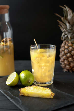 vertical frame. Fruit and pineapple lemonade drink on black background with iceの写真素材