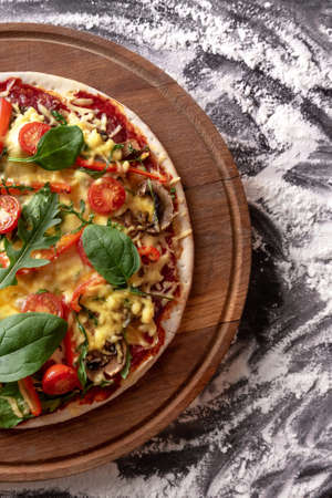 pizza on a wooden board with basil mushrooms tomatoes top viewの写真素材