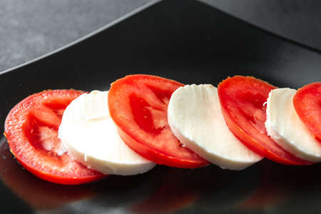 Ingredients for Caprese salad on a black plate. Tomatoes and mozzarella cheese slicedの写真素材