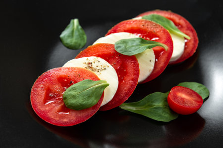 Caprese salad with olive oil tomatoes and mozzarella cheese and black pepper. Italian salad on a black plate with cheese and tomatoes. European Cuisine.の写真素材