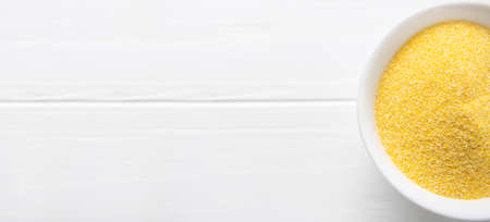 A pile of polenta or cornmeal in a white bowl. Ground dried corn or corn grits. Top view, copy place. Healthy cereal conceptの写真素材