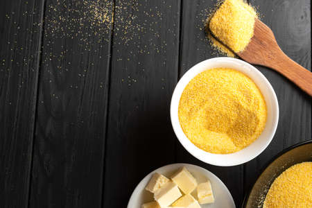 Polenta or Cornmeal Flour. Ground Dried Corn or Corn Grits in a white bowl and wooden spoon close-up on dark background. Copy spaceの写真素材
