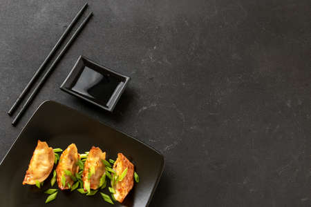 Gyoza or Jiaozi Asian fried dumplings with soy sauce, and green onions on a background of black concrete, top viewの写真素材