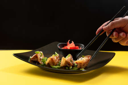 A mans hand picks up a Japanese fried dumpling with Chinese chopsticks. Asian foodの写真素材