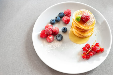 Pancakes on a white plate on a light background with berries and honey. Blank space for textの写真素材