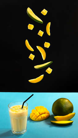 Milk drink on black background with mango. A classic mango milkshake - Lassi. A traditional drink in India from the heat. Top view. Lassi is a popular traditional dahi, yogurt based cold drink in India. Lassi consists of yogurt, water, spices and sometimes fruit and ice. Mango slices fall off. Fruit levitating in the airの写真素材