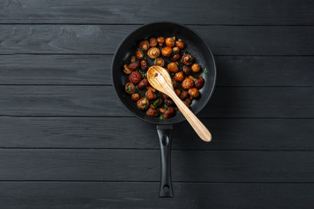 Pan of fried mushrooms champignons on a dark wooden background. Top view. Place for text and copy...