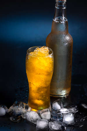 Beer cocktail in a beer glass on a black background with pieces of ice next to a beer bottle with no inscriptions. A refreshing summer cocktail.の写真素材